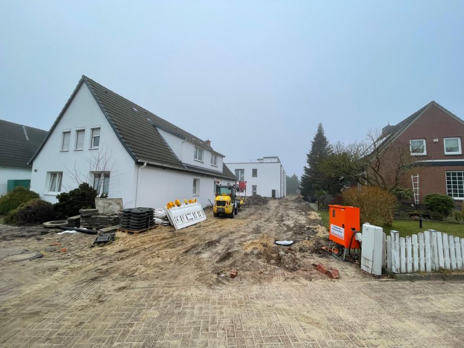 Bauwüste mit unebener Fläche, Baumaschinen und Baustellenschildern, umgeben von Häusern.