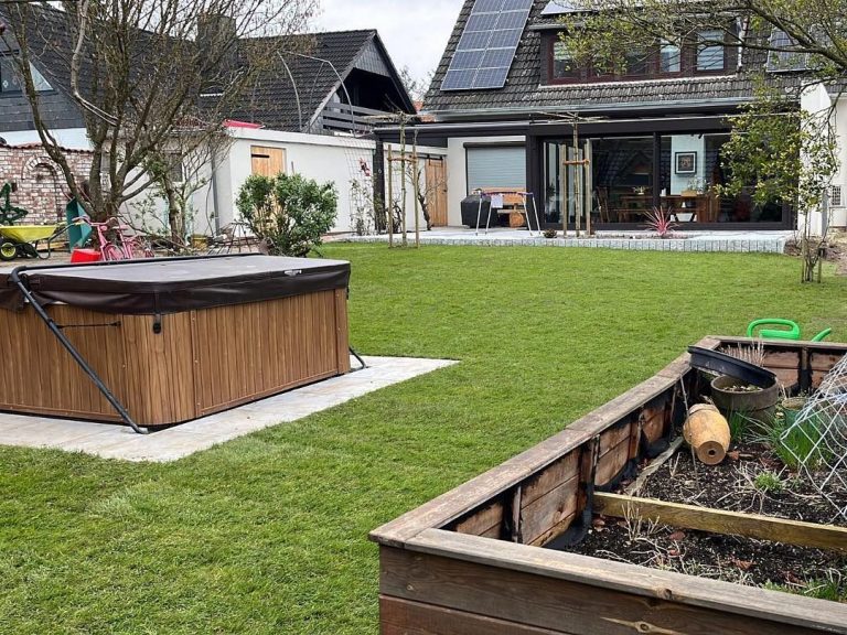 Garten mit einem Holzpool und einem bepflanzten Hochbeet im Vordergrund.